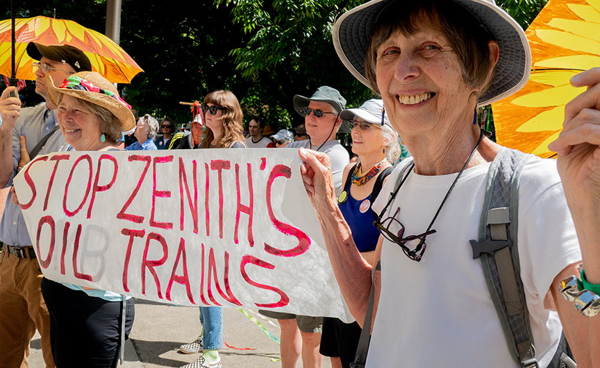 Activista sosteniendo una pequeña pancarta que dice: "Detengan los trenes petroleros Zenith".